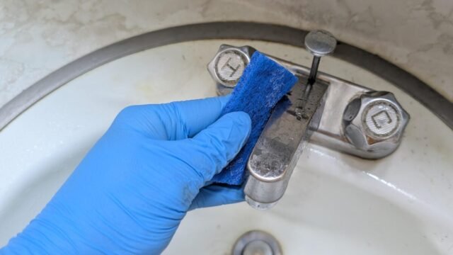 gloved-hand-scrubbing-dirty-bathroom-sink-faucet-with-blue-scouring-pad.jpg