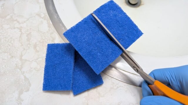 gloved-hand-using-scissors-to-cut-apart-a-blue-scouring-pad.jpg